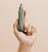 Hand holding a green Meridian branded electric nose and ear hair trimmer against a beige background.
