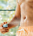 Man wearing orange swim trunks applying sunscreen spray to torso, summer skincare, sun protection outdoors