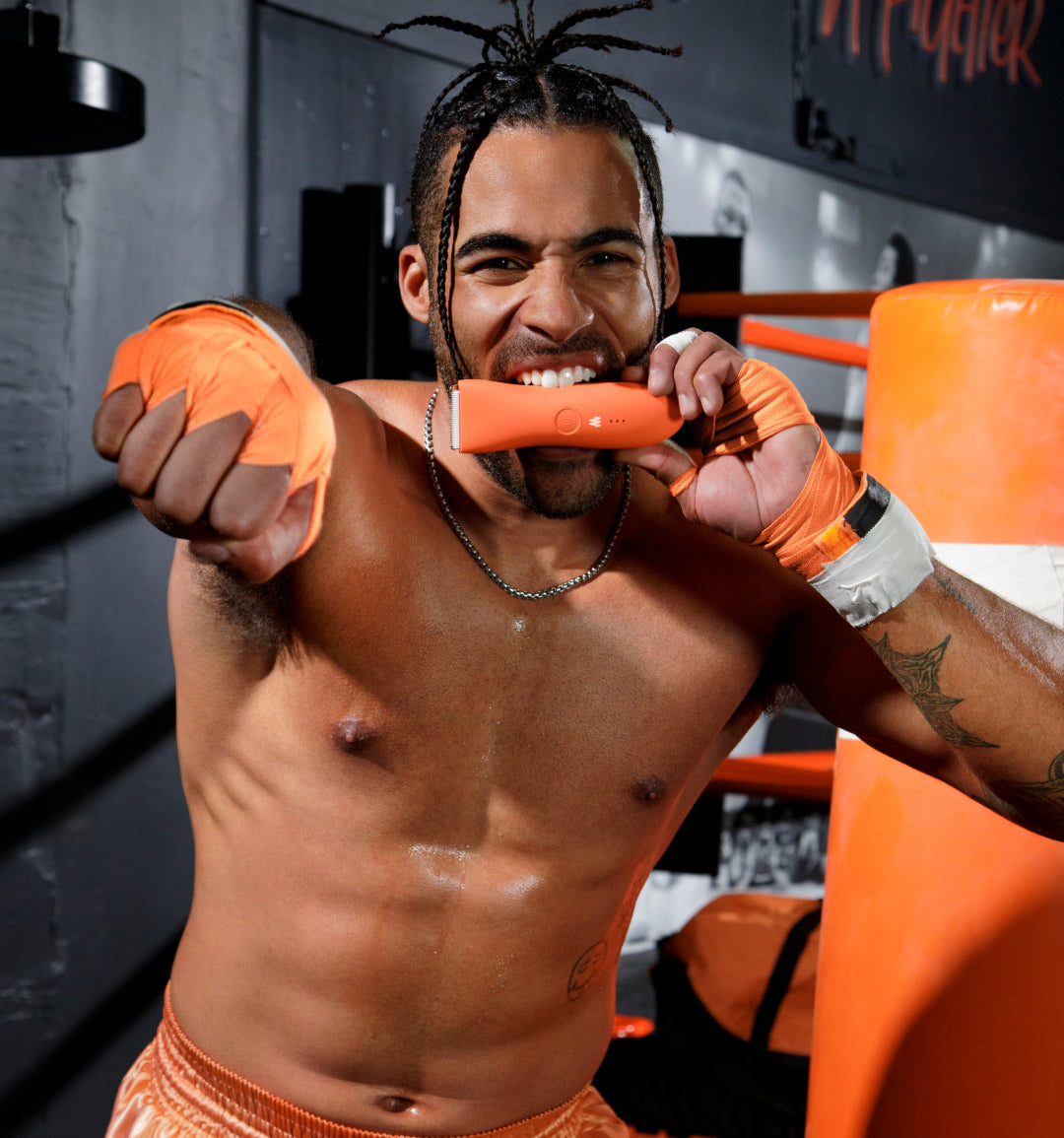 Muscular man with dreadlocks wearing orange boxing gloves and shorts training at a gym punching orange pads.